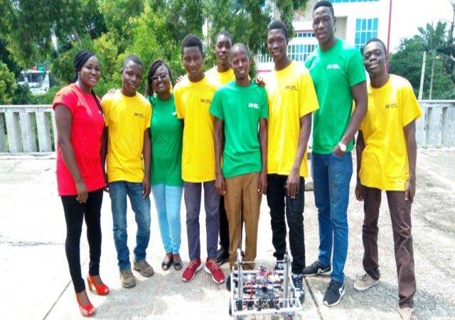 Une dizaine de jeunes en t-shirts jaunes, verts et rouges posent en extérieur avec un robot de compétition posé au sol devant eux