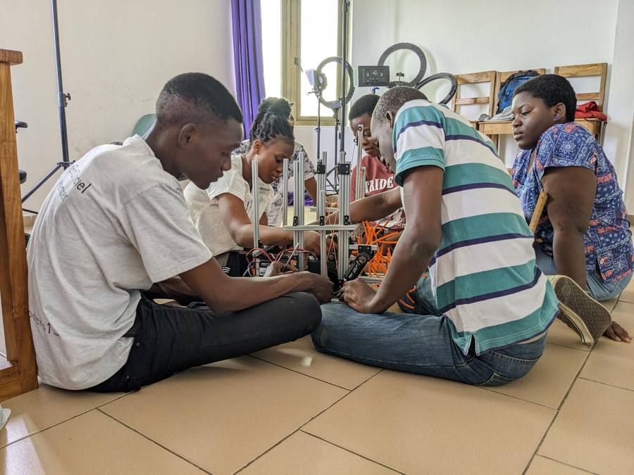 Plusieurs jeunes assis au sol assemblent la structure métallique d'un robot de compétition, entourés de câbles et de pièces