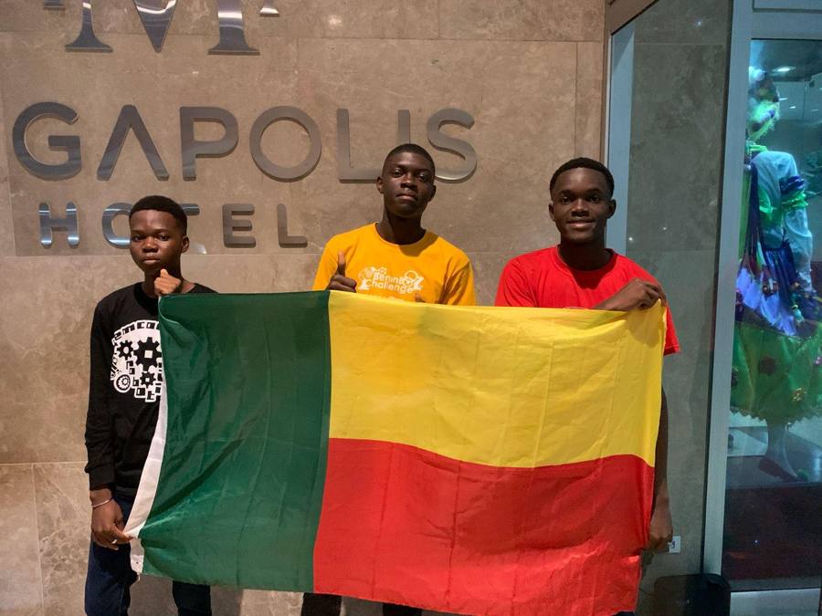 Trois jeunes de la Team Benin déploient un grand drapeau du Bénin devant l'enseigne d'un hôtel à Panama City