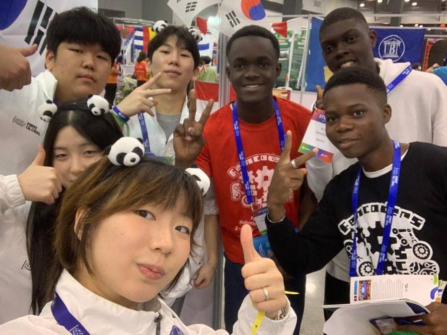 Des membres de la Team Benin posent avec des participants d'autres délégations, pouces levés et sourires, dans le hall du FIRST Global Challenge